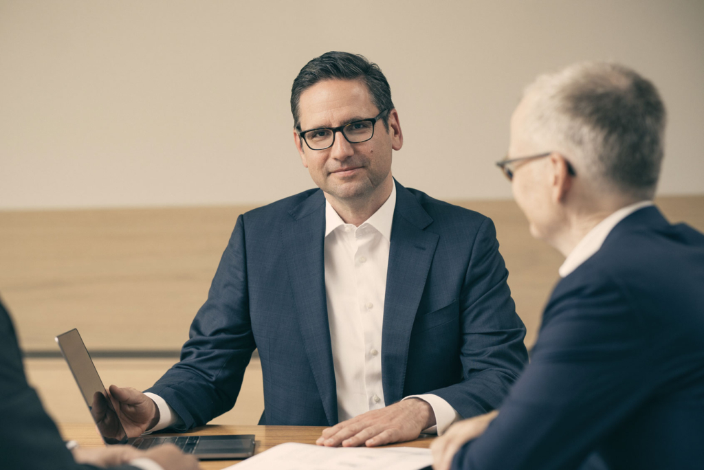 Man in suit sitting on desk watching into the camera